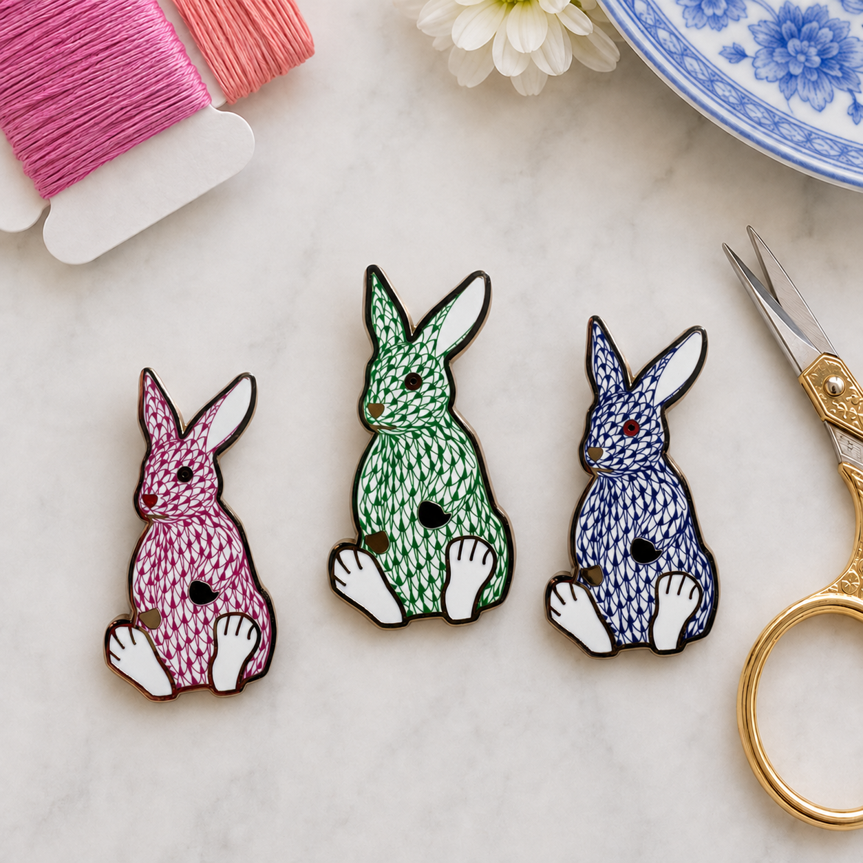 The Palm Bunny trio in pink, green and blue, styled with embroidery thread and gold scissors