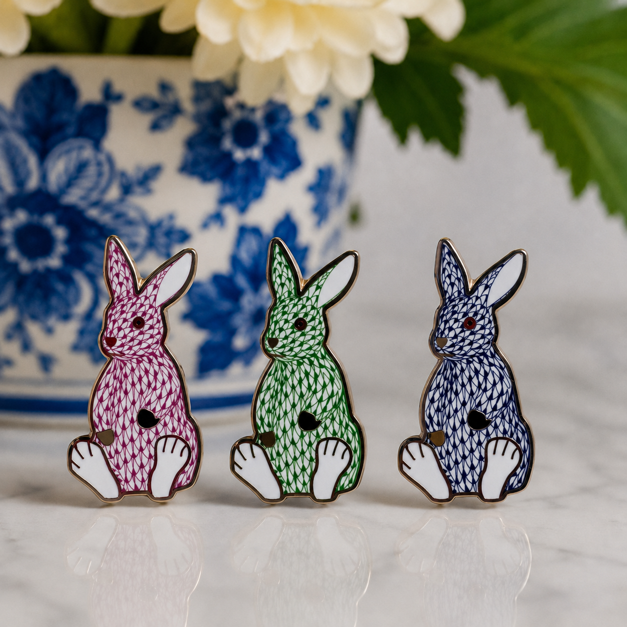 The Palm Bunny Collection: pink, green and navy enamel needle minders arranged in front of blue-and-white porcelain
